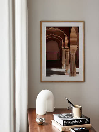 Framed architectural print with arches and columns above a wooden table with books and decor.
