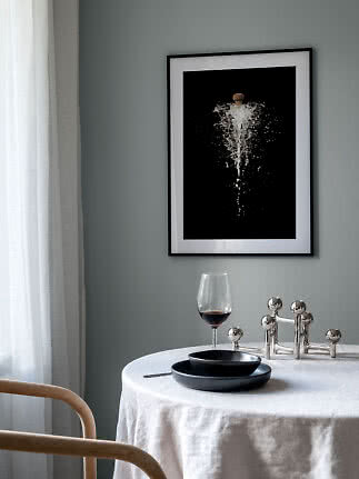 Indrammet plakat med champagneprop og sprøjt over et dækket bord med vinglas og sorte tallerkener
