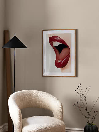 Affiche encadrée de lèvres rouges sur mur beige au-dessus d'un fauteuil crème