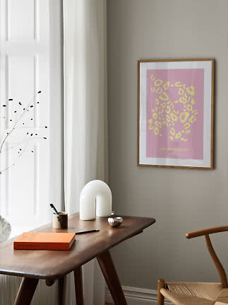 Inramad poster med rosa bakgrund och gult abstrakt mönster ovanför ett träskrivbord.