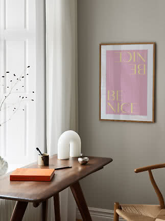 Framed pink poster with yellow text on a beige wall above a wooden desk