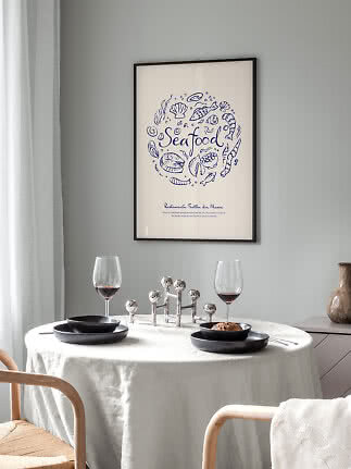 Spisebord med sort service, to vinglas og indrammet seafood-plakat på grå væg