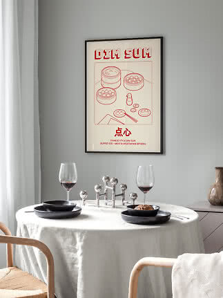 Gerahmtes Dim-Sum-Poster über rundem Esstisch mit schwarzen Tellern und zwei Weingläsern.