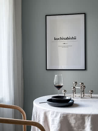 Inramad typografisk poster ovanför ett runt bord med vinglas, svarta tallrikar och ljusstake.