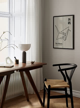 Minimalistisk hjemmekontor med træbord, sort stol, bordlampe og indrammet origami-plakat.