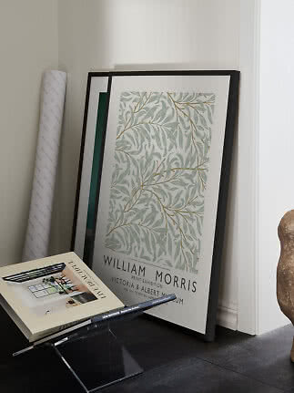 Indrammet William Morris-plakat med bladmotiv lænet op ad væggen ved siden af bøger