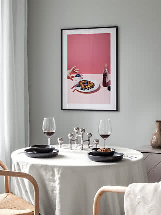 Esstisch mit schwarzem Geschirr, Weingläsern und Kerzenständer unter gerahmtem Food-Poster an grauer Wand