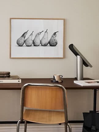 Skrivebord med stol, lampe og indrammet sort-hvid plakat med fem pærer på væggen
