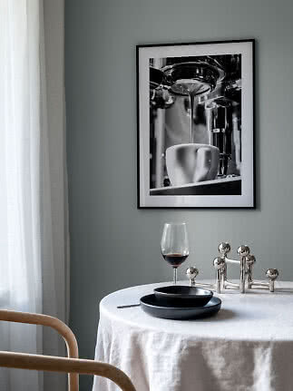 Indrammet sort-hvid plakat af espressomaskine over rundt spisebord med vinglas og sorte tallerkener