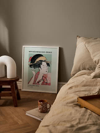 Chambre avec linge de lit beige, affiche d’art japonais au sol et lampe blanche sur tabouret