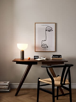 Wooden desk with black chair, lit table lamp, open notebook and framed wall art