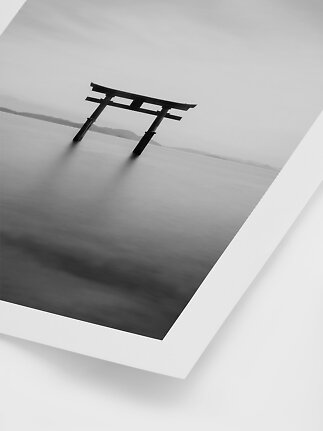 Black and white print of a Japanese torii gate in calm water with a misty horizon