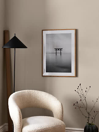 Minimalist room corner with a cream armchair, black floor lamp, and framed black-and-white print.