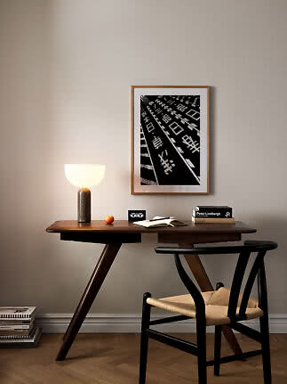 Escritorio de madera con silla negra, lámpara de mesa y póster en blanco y negro en pared beige