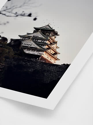Photo encadrée d’un château japonais en lumière chaude derrière un mur de pierre