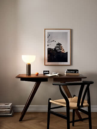 Bureau en bois foncé avec chaise noire, lampe de table et photo encadrée sur mur clair