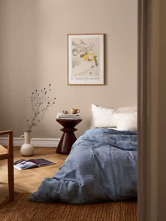 Gemütliches Schlafzimmer mit blauer Bettdecke, weißen Kissen, Beistelltisch, Vase und gerahmtem Poster