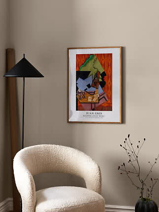 Poster incorniciato di Juan Gris su parete beige sopra una poltrona bouclé bianca accanto a lampada nera