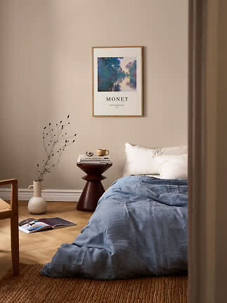 Bedroom with blue duvet, white pillows and framed Monet poster on a beige wall