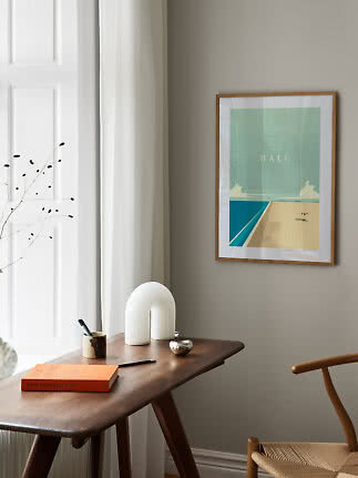 Gerahmtes Bali-Poster an beigefarbener Wand über dunklem Holztisch in hellem Interieur