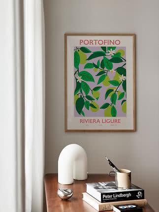 Framed Portofino poster with green pears and leaves on a beige wall above a wooden table