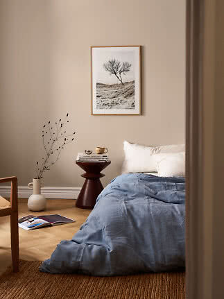 Accogliente camera da letto con biancheria blu, tavolino, vaso e stampa con albero su parete beige