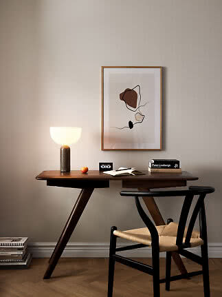 Dunkler Holzschreibtisch mit leuchtender Tischlampe, Stuhl und abstraktem Wandbild
