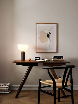 Dark table lamp with white glass shade on a wooden desk in a minimalist interior.