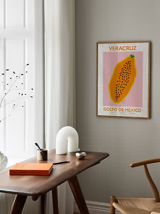Framed Veracruz poster with papaya illustration above a wooden desk in a bright modern room