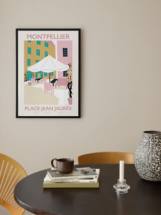 Gerahmtes Montpellier-Poster mit Cafészene an beigefarbener Wand über rundem Tisch