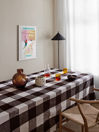 Dining table with brown check tablecloth, glasses and vase in a bright room with black floor lamp
