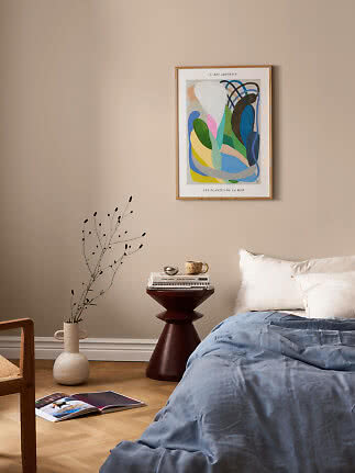 Schlafzimmer mit abstraktem Wandbild, blauer Bettdecke, rundem Beistelltisch und Bodenvase