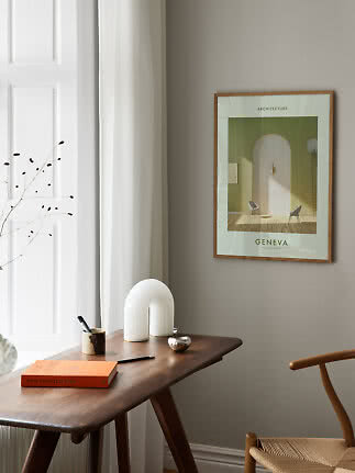 Framed architecture poster on a beige wall above a wooden desk beside white curtains