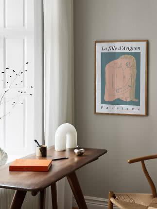 Framed art print on wall above a wooden desk by a window in a calm modern interior