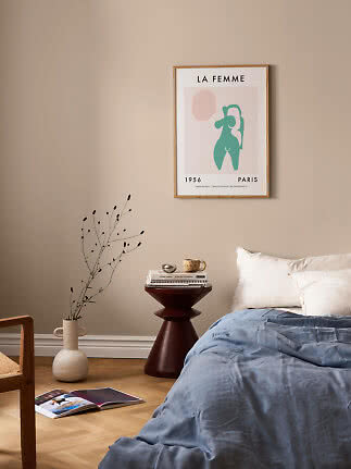 Framed abstract poster above bed in beige bedroom with side table, vase, and blue duvet