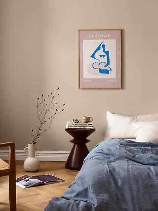 Bedroom with framed art poster on beige wall above side table and bed with blue duvet