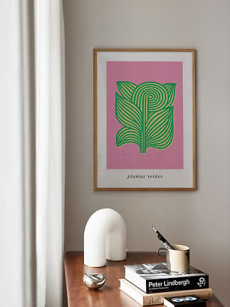 Poster incorniciato con illustrazione botanica verde su sfondo rosa sopra un tavolo in legno
