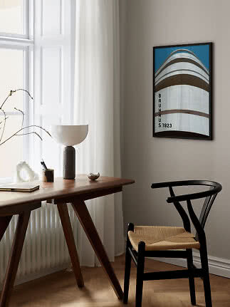 Framed Bauhaus 1923 poster on wall above desk and black chair in a bright room