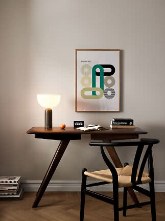 Schreibtisch mit leuchtender Tischlampe, Buch, Stuhl und gerahmtem Bauhaus-Poster an der Wand