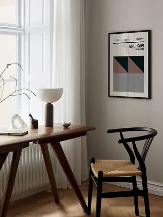 Inramad Bauhaus-affisch över ett träskrivbord vid fönstret med svart stol