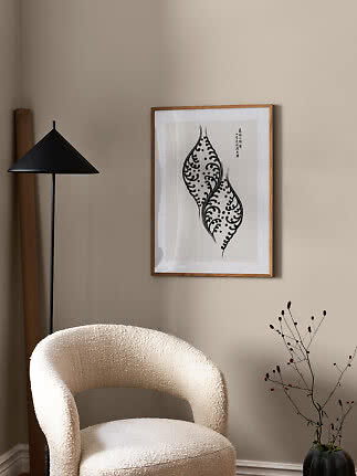 Minimalistische Zimmerecke mit cremefarbenem Sessel, schwarzer Stehlampe und gerahmtem Grafikdruck.