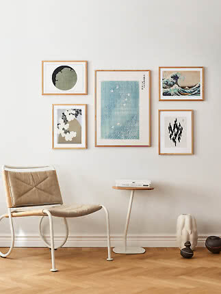 Minimalist room corner with lounge chair, side table, and five framed art prints on a light wall.