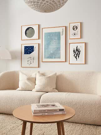 Soggiorno minimalista con divano color crema, tavolino in legno e parete con cinque stampe incorniciate.