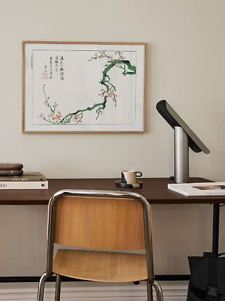 Desk with wooden chair, table lamp and framed floral branch print on the wall