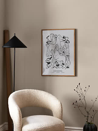Indrammet sort-hvid hesteplakat på beige væg over en cremefarvet lænestol ved sort gulvlampe