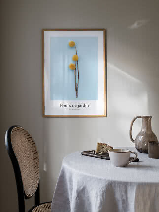 Ingelijste botanische poster met gele bloemen op blauwe achtergrond boven een gedekte tafel