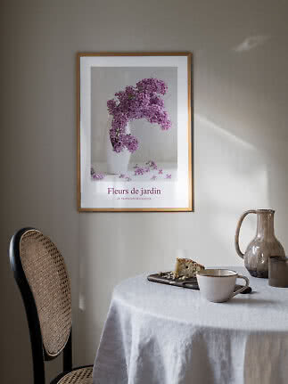 Ingelijste bloemenposter met paarse seringen in witte vaas boven een gedekte tafel
