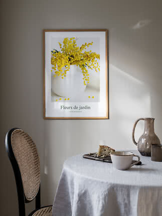 Ingelijste bloemenposter met gele mimosa in witte vaas boven een gedekte tafel