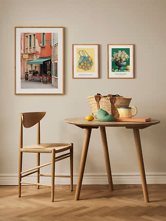Essecke mit Holzstuhl, rundem Tisch, Korbtasche, Becher und drei gerahmten Kunstdrucken an der Wand