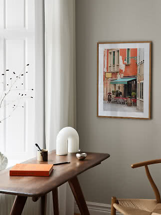 Framed photo of a café facade with green awning above a wooden desk in a bright room